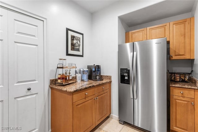 kitchen featuring light tile patterned flooring, stainless steel fridge, and dark stone counters