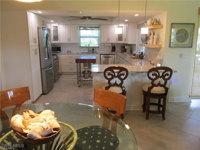 kitchen featuring a kitchen bar, white cabinetry, kitchen peninsula, backsplash, and stainless steel appliances