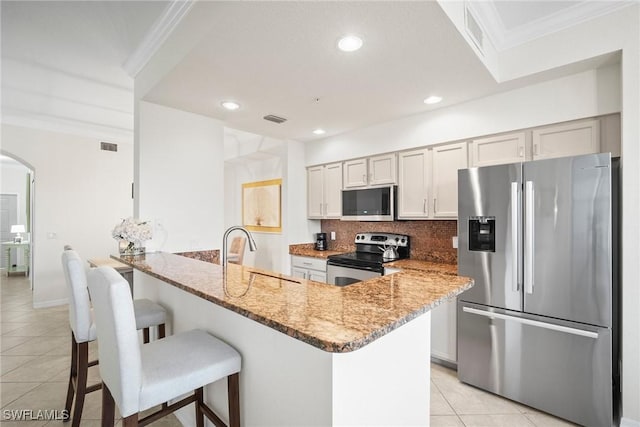 kitchen with sink, a breakfast bar area, light stone counters, light tile patterned floors, and appliances with stainless steel finishes