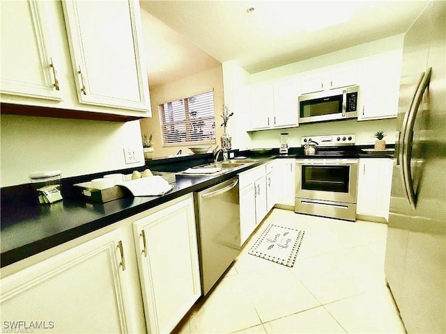 kitchen featuring dark countertops, appliances with stainless steel finishes, light tile patterned flooring, white cabinetry, and a sink