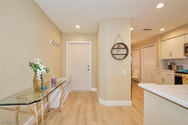 kitchen with white cabinets, light hardwood / wood-style flooring, stainless steel appliances, and tasteful backsplash