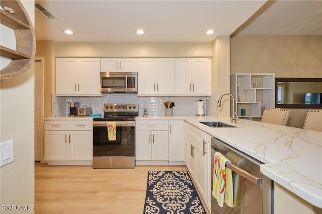 kitchen with light stone countertops, white cabinetry, sink, and stainless steel appliances