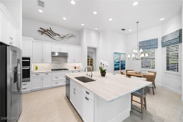 kitchen featuring appliances with stainless steel finishes, sink, white cabinets, hanging light fixtures, and a center island with sink