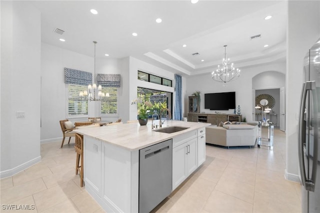 kitchen with an inviting chandelier, appliances with stainless steel finishes, a kitchen island with sink, and white cabinets