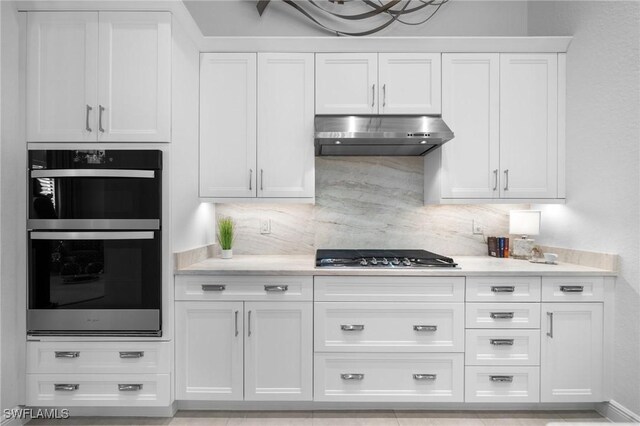 kitchen with white cabinetry, multiple ovens, stainless steel gas stovetop, and decorative backsplash