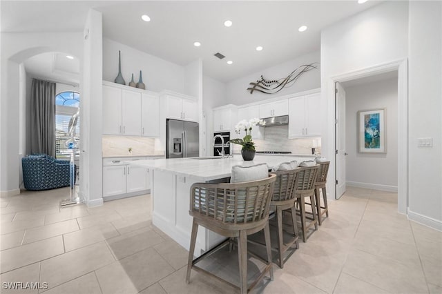 kitchen with white cabinetry, stainless steel fridge with ice dispenser, an island with sink, and a breakfast bar