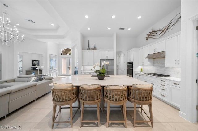 kitchen with a breakfast bar area, appliances with stainless steel finishes, white cabinets, a large island, and a high ceiling