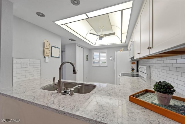 kitchen with a skylight, white cabinetry, sink, light stone counters, and white appliances