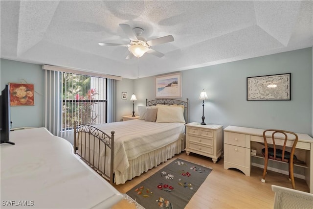 bedroom with a raised ceiling, ceiling fan, a textured ceiling, and light hardwood / wood-style flooring