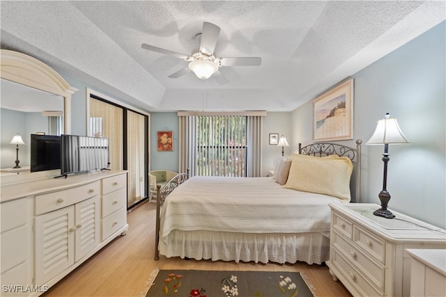 bedroom with a raised ceiling, ceiling fan, a textured ceiling, and light hardwood / wood-style flooring