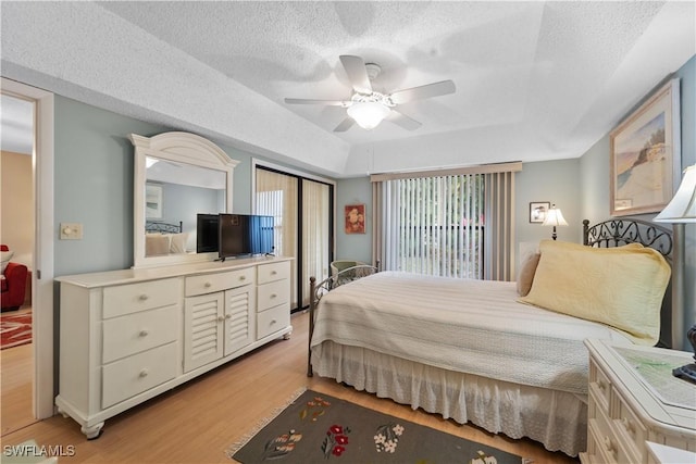 bedroom with a raised ceiling, ceiling fan, a textured ceiling, and light hardwood / wood-style floors