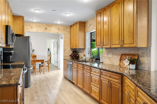 kitchen featuring sink, light hardwood / wood-style flooring, dark stone counters, and appliances with stainless steel finishes