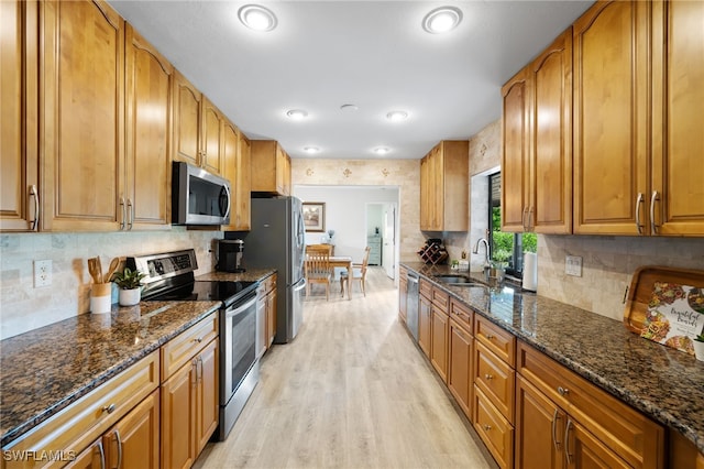 kitchen featuring tasteful backsplash, dark stone counters, sink, light hardwood / wood-style flooring, and stainless steel appliances