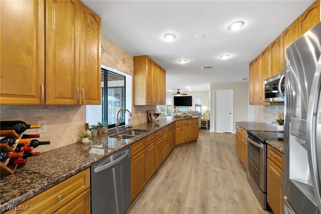 kitchen featuring appliances with stainless steel finishes, decorative backsplash, light wood-type flooring, dark stone countertops, and sink