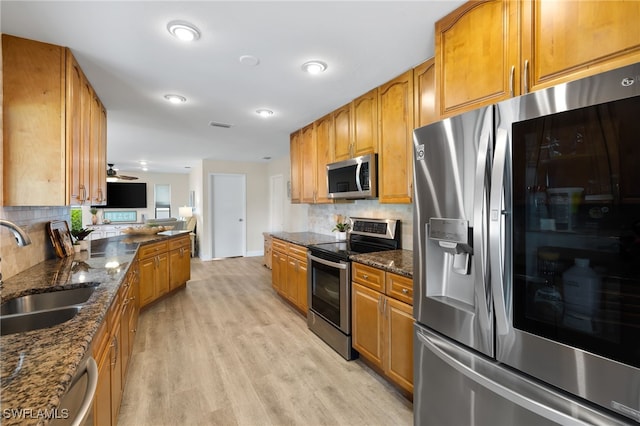 kitchen featuring sink, light hardwood / wood-style flooring, dark stone countertops, and stainless steel appliances