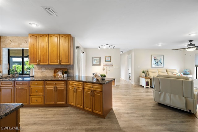 kitchen with dark stone countertops, decorative backsplash, kitchen peninsula, light wood-type flooring, and ceiling fan