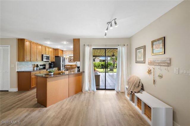 kitchen with kitchen peninsula, backsplash, light wood-type flooring, dark stone countertops, and stainless steel appliances