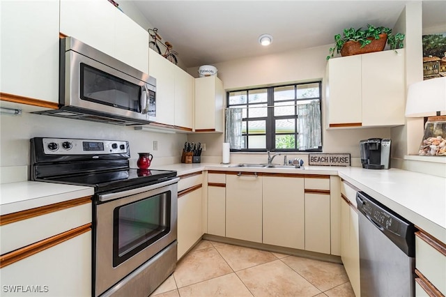 kitchen featuring stainless steel appliances, light tile patterned flooring, sink, and white cabinetry