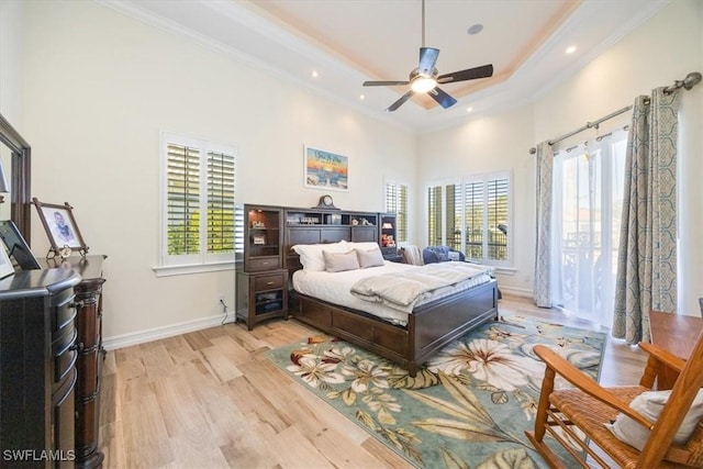 bedroom featuring ornamental molding, a tray ceiling, light hardwood / wood-style floors, and multiple windows