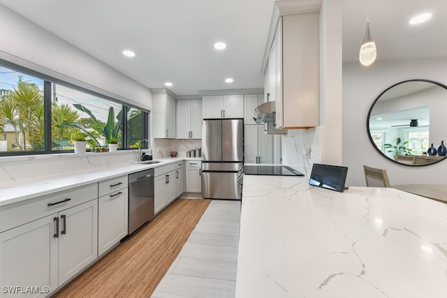 kitchen featuring hanging light fixtures, sink, white cabinets, light stone countertops, and stainless steel appliances