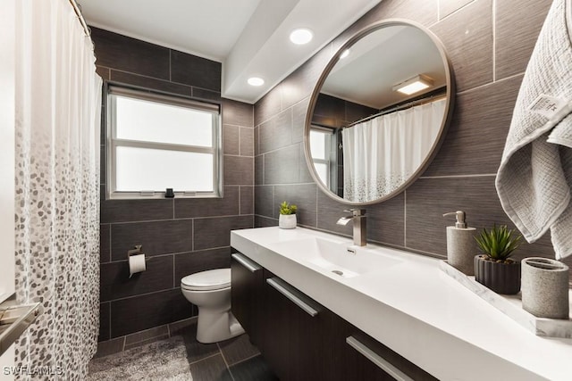 bathroom with toilet, vanity, tile patterned floors, and tile walls