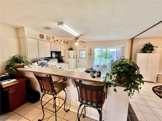 kitchen with white appliances, white cabinetry, light tile patterned floors, kitchen peninsula, and a breakfast bar area