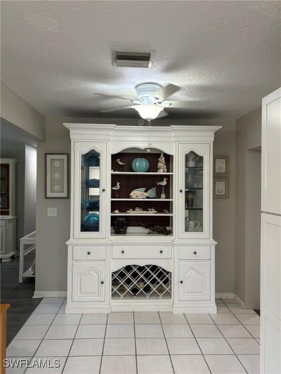 bar with ceiling fan, white cabinetry, a textured ceiling, and light tile patterned flooring