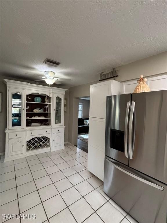 kitchen with light tile patterned flooring, white cabinets, a textured ceiling, and stainless steel fridge with ice dispenser