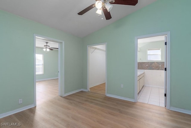 unfurnished bedroom featuring multiple windows, a walk in closet, lofted ceiling, and light hardwood / wood-style floors