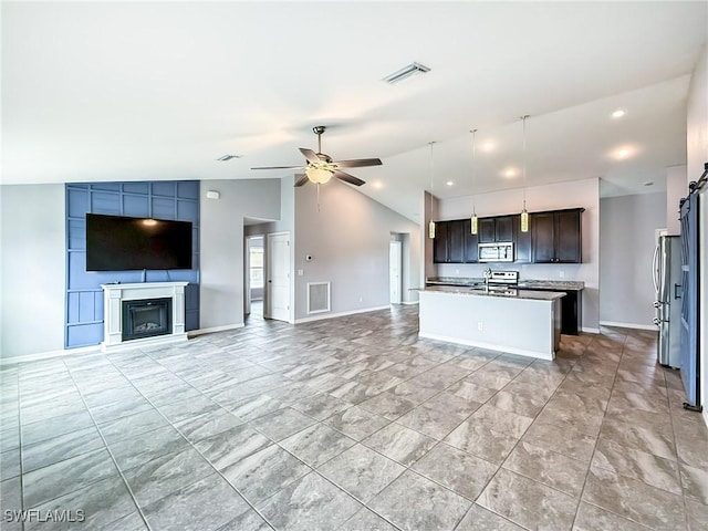 kitchen featuring vaulted ceiling, ceiling fan, a barn door, dark brown cabinets, and a center island with sink