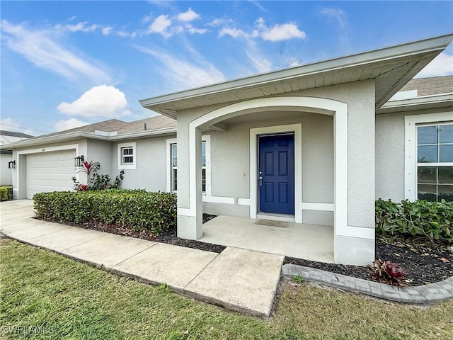 view of exterior entry with an attached garage, a shingled roof, and stucco siding