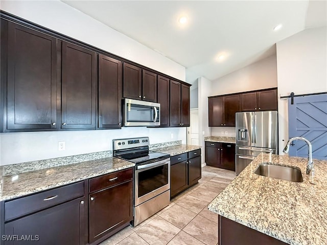 kitchen featuring sink, dark brown cabinets, stainless steel appliances, light stone countertops, and a barn door