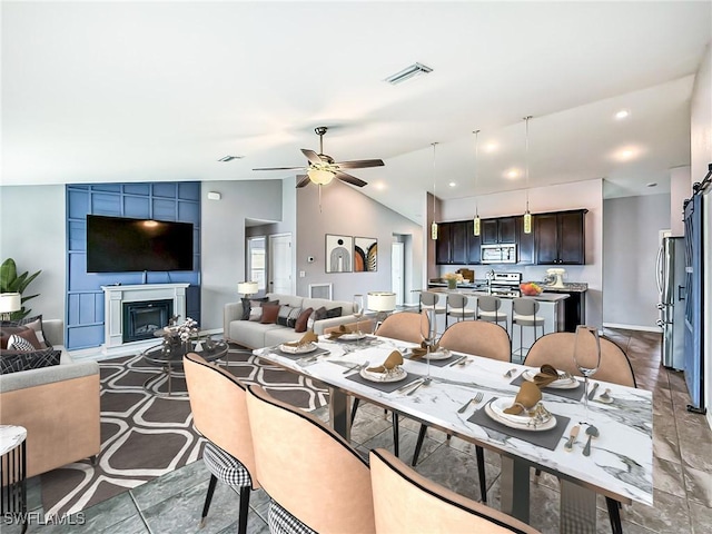 dining area with visible vents, vaulted ceiling, a ceiling fan, and a glass covered fireplace