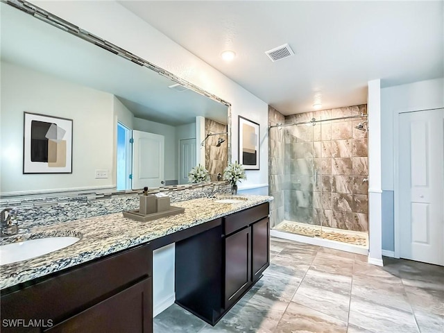 bathroom with a tile shower, double vanity, a sink, and visible vents