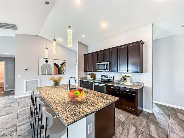 kitchen featuring light stone counters, appliances with stainless steel finishes, a kitchen island with sink, a sink, and dark brown cabinets