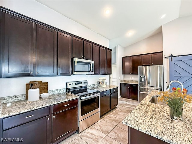 kitchen with a barn door, lofted ceiling, appliances with stainless steel finishes, dark brown cabinets, and a sink