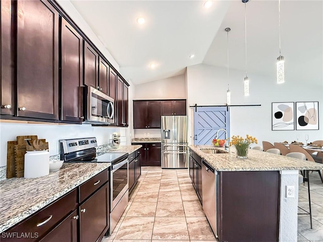 kitchen featuring hanging light fixtures, a barn door, appliances with stainless steel finishes, a sink, and a kitchen breakfast bar