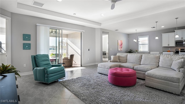 tiled living room featuring a tray ceiling and a notable chandelier