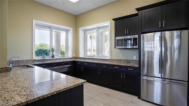 kitchen featuring stainless steel appliances, light stone countertops, sink, and a drop ceiling