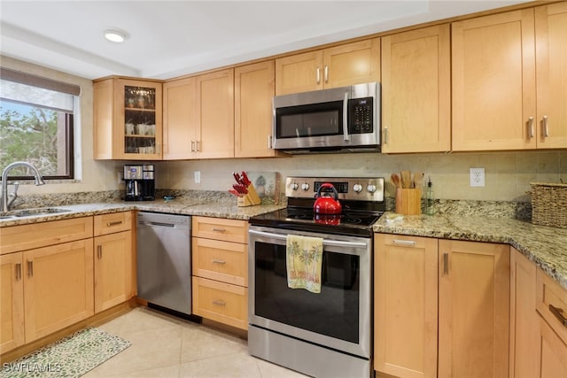 kitchen with light brown cabinets, light stone countertops, light tile patterned floors, appliances with stainless steel finishes, and a sink