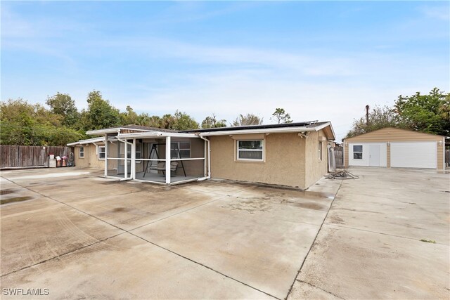 rear view of house with a garage, a sunroom, an outdoor structure, and a patio