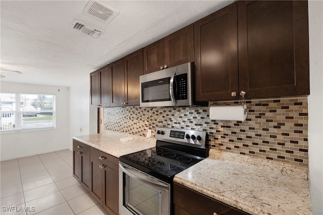 kitchen with light stone countertops, backsplash, dark brown cabinetry, and appliances with stainless steel finishes