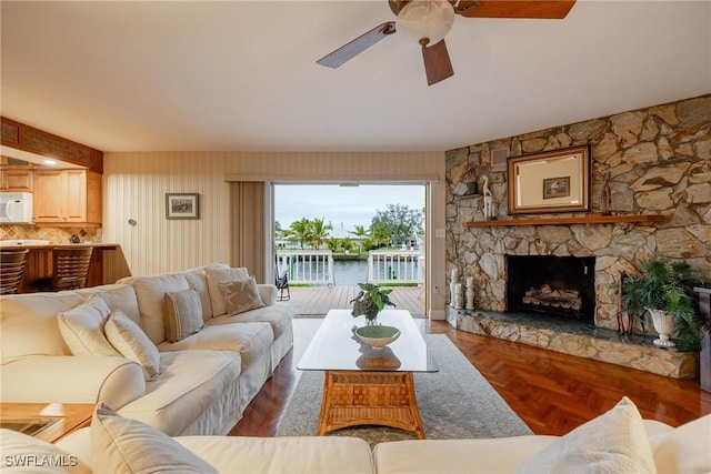 living room with a water view, a stone fireplace, and ceiling fan