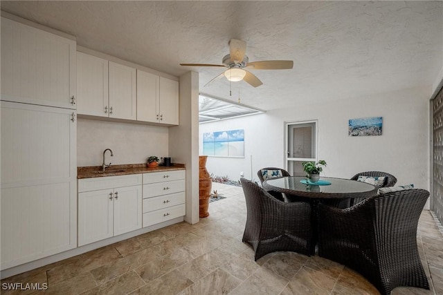 dining area with ceiling fan, sink, and a textured ceiling