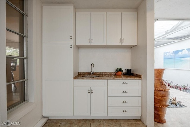 bar featuring white cabinetry, sink, and dark stone countertops