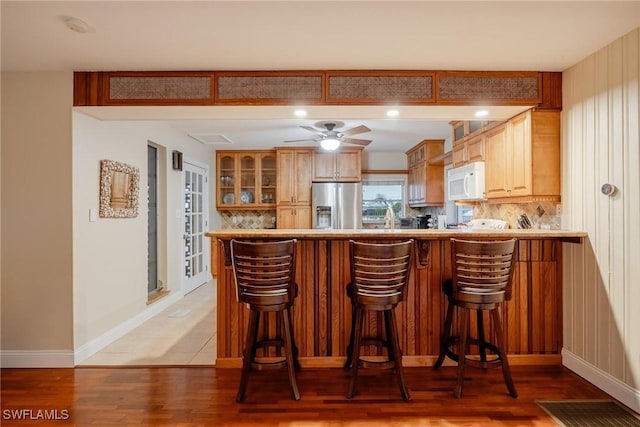 kitchen featuring stainless steel refrigerator with ice dispenser, tasteful backsplash, a kitchen breakfast bar, kitchen peninsula, and hardwood / wood-style floors