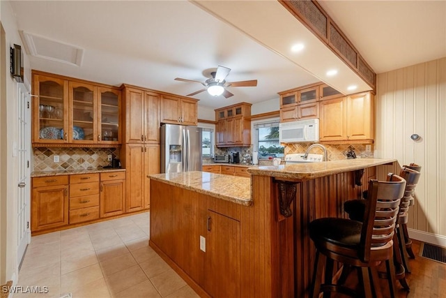 kitchen with ceiling fan, a kitchen breakfast bar, light stone countertops, stainless steel fridge with ice dispenser, and kitchen peninsula