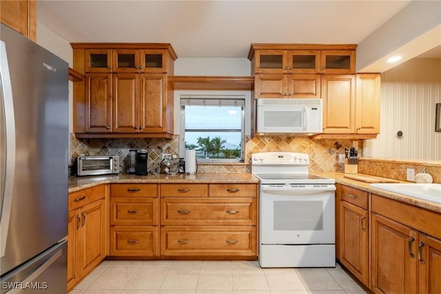 kitchen featuring tasteful backsplash, white appliances, light stone counters, and light tile patterned floors