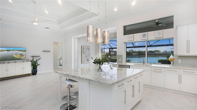 kitchen featuring a water view, decorative light fixtures, a center island, a tray ceiling, and white cabinets