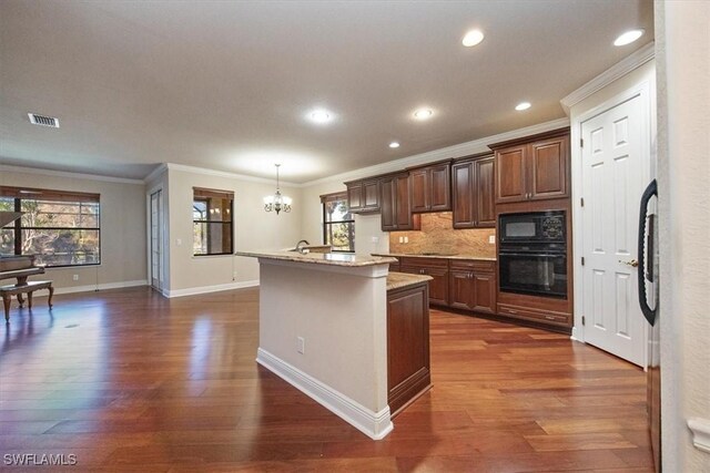 kitchen with hanging light fixtures, an island with sink, a notable chandelier, decorative backsplash, and black appliances